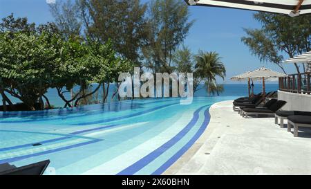 Luxuriöser Infinity-Pool mit Blick auf das Meer im tropischen Resort, mit komfortablen Liegestühlen unter Sonnenschirmen und üppigem Grün. Exotische Reisen und Leisu Stockfoto