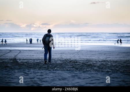 Mann, der am Piha Beach läuft. Nicht erkennbare Leute, die am Strand spielen. Auckland. Stockfoto