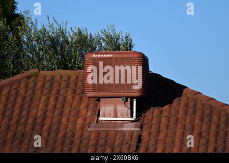 Rötlich-braune Breezair-Verdunstungskühleinheit auf dem Keramikdach eines Vorstadthauses an einem sonnigen Tag Stockfoto