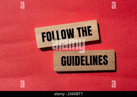 Folgen Sie den Hinweisen auf Holzblöcken mit rotem Hintergrund. Konzeptionell Befolgen Sie das Richtliniensymbol. Kopierbereich. Stockfoto