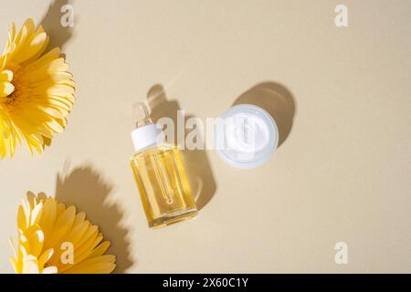 Kosmetisches Serum und Creme, gelbe Gerbera-Blüten auf neutralem Hintergrund im Sonnenlicht. Draufsicht, flach, Kopierbereich. Stockfoto