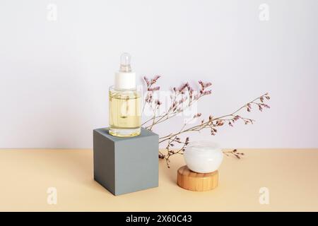 Kosmetisches Serum und Creme im Glas und violette Kermek-Blüten auf beigefarbenem Tisch. Naturkosmetik-Konzept. Nahaufnahme. Stockfoto