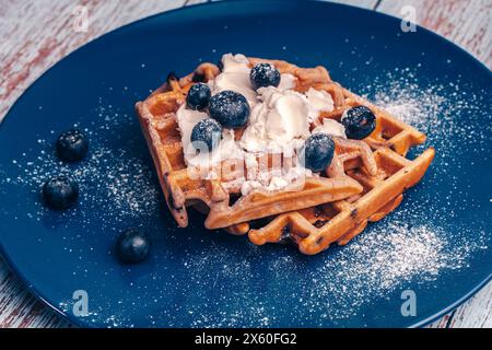 Belgische Waffeln mit Blaubeeren, Hüttenkäse und Eis auf einem blauen Teller. Traditionelles Dessert. Nahaufnahme. Hochwertige Fotos Stockfoto