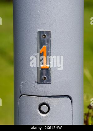 Nahaufnahme eines metallischen Stabs mit der Zahl 1 in leuchtendem Orange vor grauem Hintergrund. Stockfoto