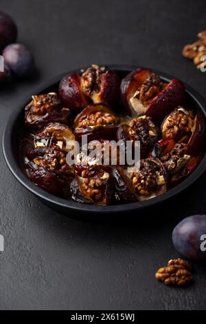 Pflaumen gebacken mit Camembert-Käse, Walnüssen und Honig auf einem schwarzen Teller. Beliebte heiße Vorspeise. Selektiver Fokus, Nahaufnahme. Stockfoto
