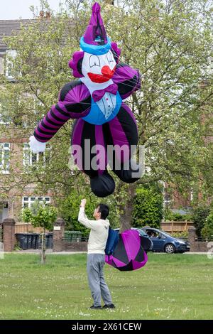 London, Großbritannien. 12. Mai 2024. Ein Mann unter einem riesigen Clowndrachen, der von Simon Hennessy von Brighton Kite Flyers geflogen wurde, als Drachenflieger am 23. Streatham Common Kite Day teilnehmen. Die beliebte Veranstaltung bringt Kite-Enthusiasten nach Streatham Common, darunter Experten und Familien, die einen Tag ausklingen möchten. Quelle: Stephen Chung / Alamy Live News Stockfoto