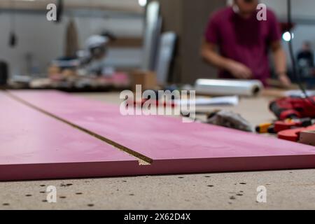 Möbelherstellung. Kante der rosafarbenen Möbelplatte in Nahaufnahme auf der Werkbank bei der Herstellung von Schrankmöbeln Stockfoto