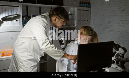 Zwei Wissenschaftler, ein Mann und eine Frau, arbeiten in einem Labor zusammen und diskutieren die Ergebnisse vor einem Computer. Stockfoto