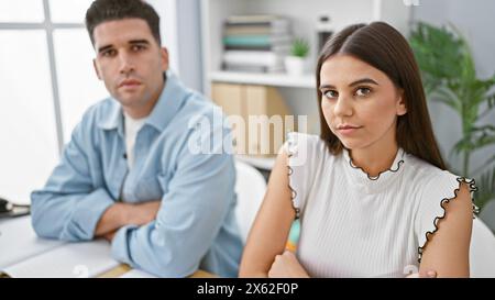 Ein seriöser Mann und eine ernste Frau mit überkreuzten Armen sitzen in einem modernen Büro und zeigen Teamarbeit in einer Unternehmensumgebung. Stockfoto