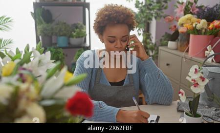 afroamerikanerin arbeitet in einem lebhaften Blumenladen, umgeben von bunten Blüten, während sie einen Anruf tätigt. Stockfoto