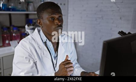 Fokussierter afrikanischer Mann mit Laborkittel, der am Computer in einer modernen Laborumgebung arbeitet. Stockfoto