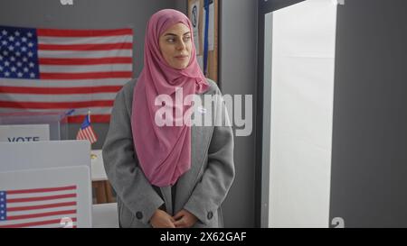 Eine junge Frau mit Hijab steht mit einem stolzen Ausdruck in einem amerikanischen Wahlzentrum und zeigt einen Aufkleber mit dem Aufdruck „ich habe gestimmt“. Stockfoto