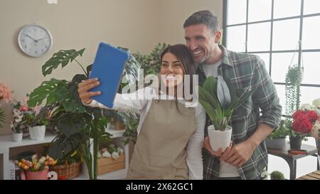 Ein Mann und eine Floristin machen zusammen ein Selfie drinnen in einem Blumenladen voller Pflanzen. Stockfoto