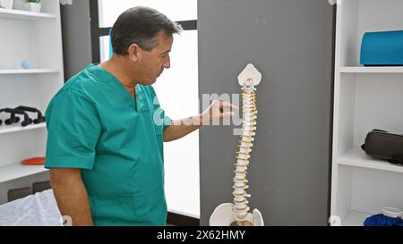 Reifer Mann in Peelings untersucht Wirbelsäulenmodell im Klinikinnenraum. Stockfoto