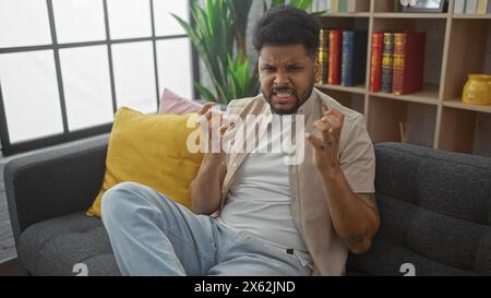 Ein afroamerikaner grimmt auf einem Sofa in einem modernen Wohnzimmer und drückt Frustration oder Unbehagen aus. Stockfoto