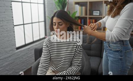 Eine Mutter flechtet die Haare ihrer Tochter in einem gemütlichen Wohnzimmer und zeigt Familie, Pflege und Leben zu Hause. Stockfoto