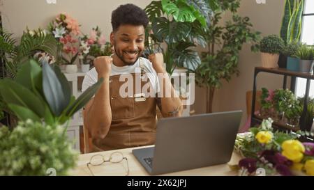 Ein aufgeregter afrikanischer Mann mit einem Laptop in einem Blumenladen, der urbanes Unternehmertum und Positivität ausstrahlt. Stockfoto