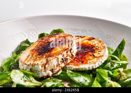 Gegrillter Ziegenkäse auf einem Bett aus frischen Spinatblättern, garniert mit balsamischer Reduktion. Stockfoto