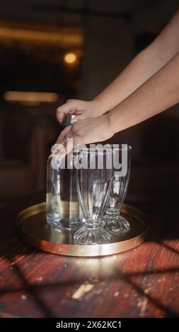 Eine Frau stellt leere Gläser auf ein Tablett und bereitet sich drinnen auf einen Getränkeservice vor. Stockfoto