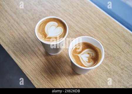 Zwei Tassen Cappuccino mit herzförmiger Latte Art auf einem Holztisch. Stockfoto