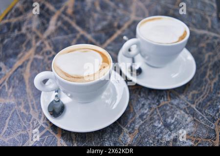 Zwei Cappuccinos in weißen Tassen auf einem Marmortisch, die eine entspannte Kaffeepause reflektieren. Stockfoto