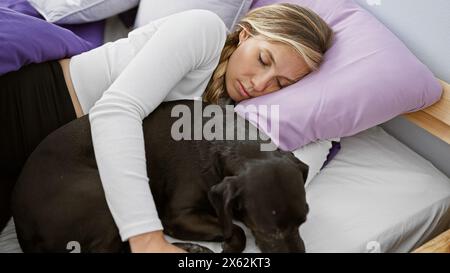 Eine junge kaukasische Frau umarmt liebevoll ihren schlafenden schwarzen labrador in einem gemütlichen Schlafzimmer, was einen friedlichen und liebevollen Moment veranschaulicht. Stockfoto