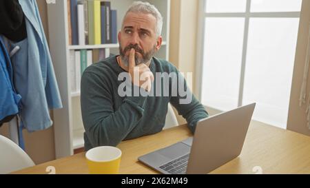 Nachdenklicher bärtiger Mann mit Laptop in einem gemütlichen Heimbüro Stockfoto