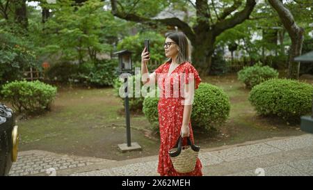 Die hispanische Frau in Brille fängt japans alte Gotokuji-Tempel mit ihrem Handy ein und genießt ihre Rolle als Tourist Stockfoto