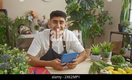 Ein lächelnder junger Mann mit einer Tafel in einem Blumenladen, umgeben von verschiedenen Pflanzen und Blumenarrangements. Stockfoto