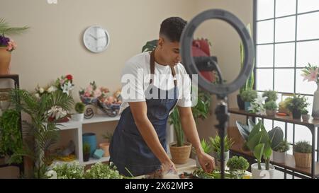Ein junger Mann arrangiert Blumen in einem überdachten Gartenladen, mit einem Ringlicht und Pflanzen im Hintergrund. Stockfoto