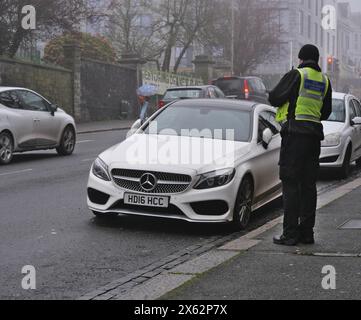 Ein Beamter, Parkwächter, überprüft Autos, die auf einer belebten Straße im Stadtzentrum geparkt sind. Plymouth, Großbritannien Stockfoto