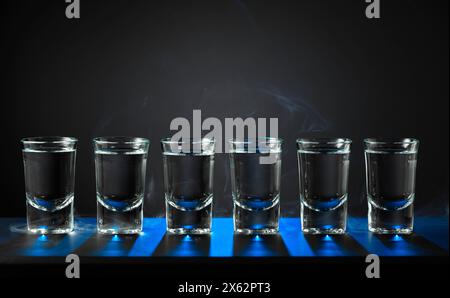 Alkoholische Aufnahmen von Wodka oder starkes Getränk in kleinen Gläsern auf schwarzem Hintergrund. Blaue Hintergrundbeleuchtung. Kopierbereich. Stockfoto