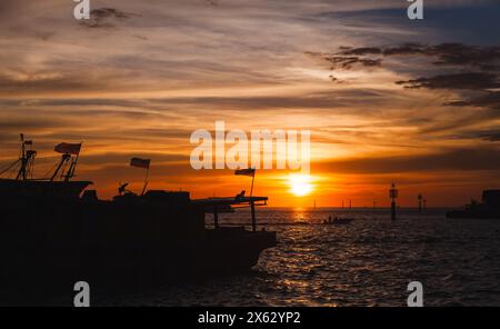 Silhuettes mit Fischerbooten mit malaysischer Flagge, die bei Sonnenuntergang auf dem KK Fish Market vor Anker liegen Stockfoto