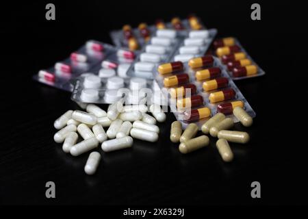 Pillen auf einem schwarzen Holztisch, Variation der Streumedikation in Kapseln. Hintergrundinformationen zu Pharmazie, Antibiotika, Vitaminen Stockfoto