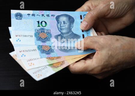 Ältere Frau mit Yuan-Banknoten in faltigen Händen. Konzept der Pensionszahlungen in China, Einsparungen im Ruhestand, chinesische Rentner mit Geld Stockfoto