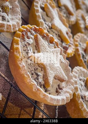 Frisch gebackene, mit Sternchen überzogene Hackpasteten, in Puderzucker bestäubt und auf einer Drahtschale gekühlt. Stockfoto