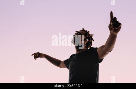 Junger Mann mit Dreadlocks tanzt in einem Studio energisch zum Takt seiner drahtlosen Playlist. Die Augen geschlossen, die Arme ausgestreckt, zeigt er seine Bewegung Stockfoto