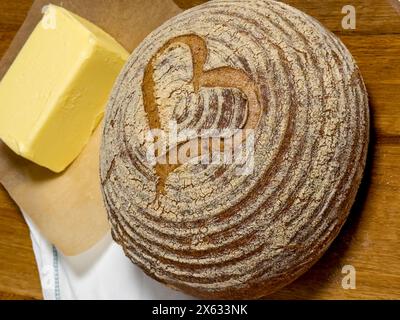 Frisch gebackene knusprige Boule mit dekorativer Herznote, serviert auf einem Holzbrett mit einem Butterblock Stockfoto