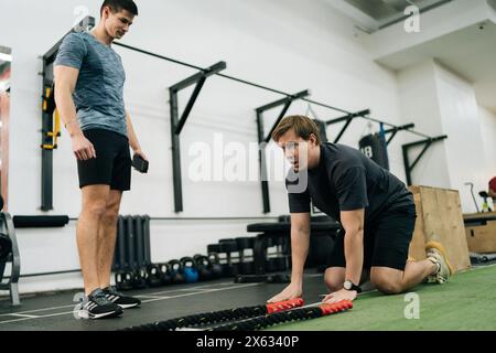 Erschöpfter Anfängersportler fällt nach dem Kampfseiltraining in der Crosstrainingshalle mit Hilfe eines Personal Trainers auf den Boden. Konzept von Stockfoto