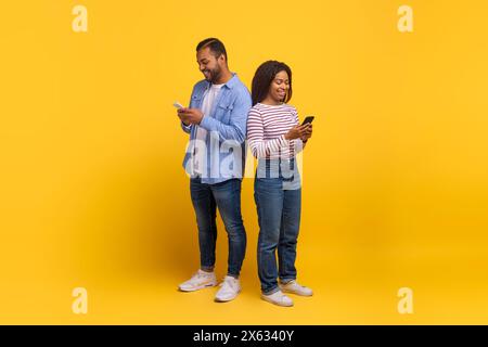 Zwei Personen stehen mit Smartphones vor gelbem Hintergrund hintereinander Stockfoto