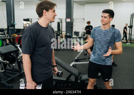 Seitenansicht eines persönlichen männlichen Trainers, der jungen Sportanfänger hilft und gemeinsam im Fitnessstudio diskutiert. Fitness-Coach männlich diskutiert Training, Workout Stockfoto