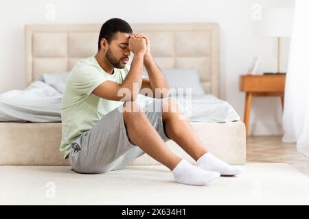 Junger Mann, der am Bett sitzt und sich gestresst oder unwohl fühlt Stockfoto