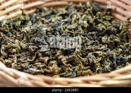 Gunpulvergrüner Tee getrocknete Blätter in rustikaler Rattanschale aus Holz. Chinesische traditionelle aromatische Getränkezutat Stockfoto
