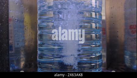 Nahaufnahme des Gießwassers mit einer 5-Liter-Kunststoff-Wasserflasche an der örtlichen Wasserfilterstation mit automatischer Wasserfiltermaschine Stockfoto