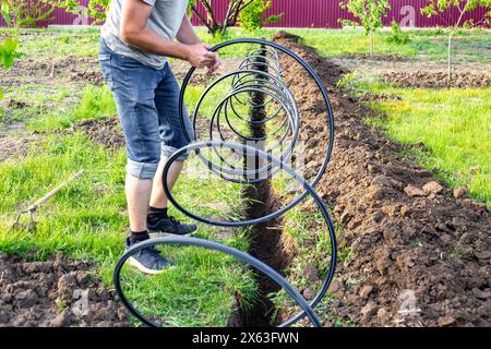 Der Mensch legt ein Kunststoffrohr auf einen Graben, um Wasser für ein Tropfbewässerungssystem zu liefern. Installation einer automatischen Tropfbewässerung für den Garten. Stockfoto