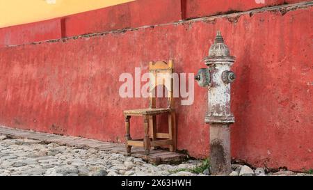 268 Rusty alter Feuerhydrant und Holzstuhl neben der roten Dado-Schiene, Kolonialhaus in der Calle Amargura Street, Plaza Mayor Square. Trinidad-Kuba. Stockfoto