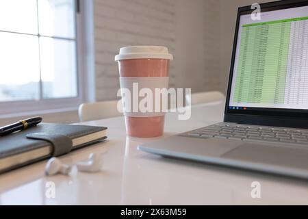 Im Büro, Laptop mit Tabellenkalkulation auf weißem Schreibtisch neben rosa Kaffeetasse Stockfoto