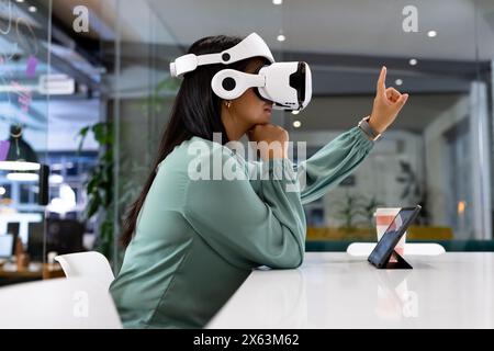 Im Büro eine Geschäftsfrau mit VR-Headset, die auf etwas zeigt Stockfoto