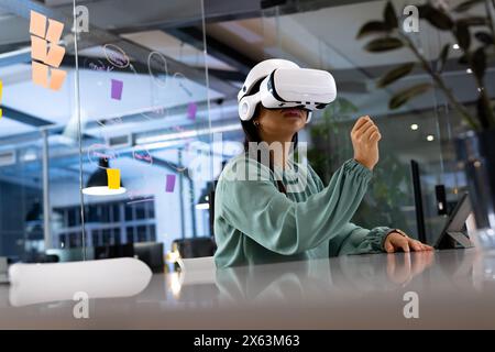 Birassische Geschäftsfrau im VR-Headset berührt die Luft und arbeitet spät im Büro Stockfoto