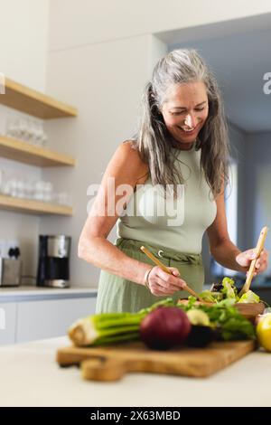 Zu Hause, reife Kaukasierin, die ärmelloses Top trägt und Essen zubereitete Stockfoto